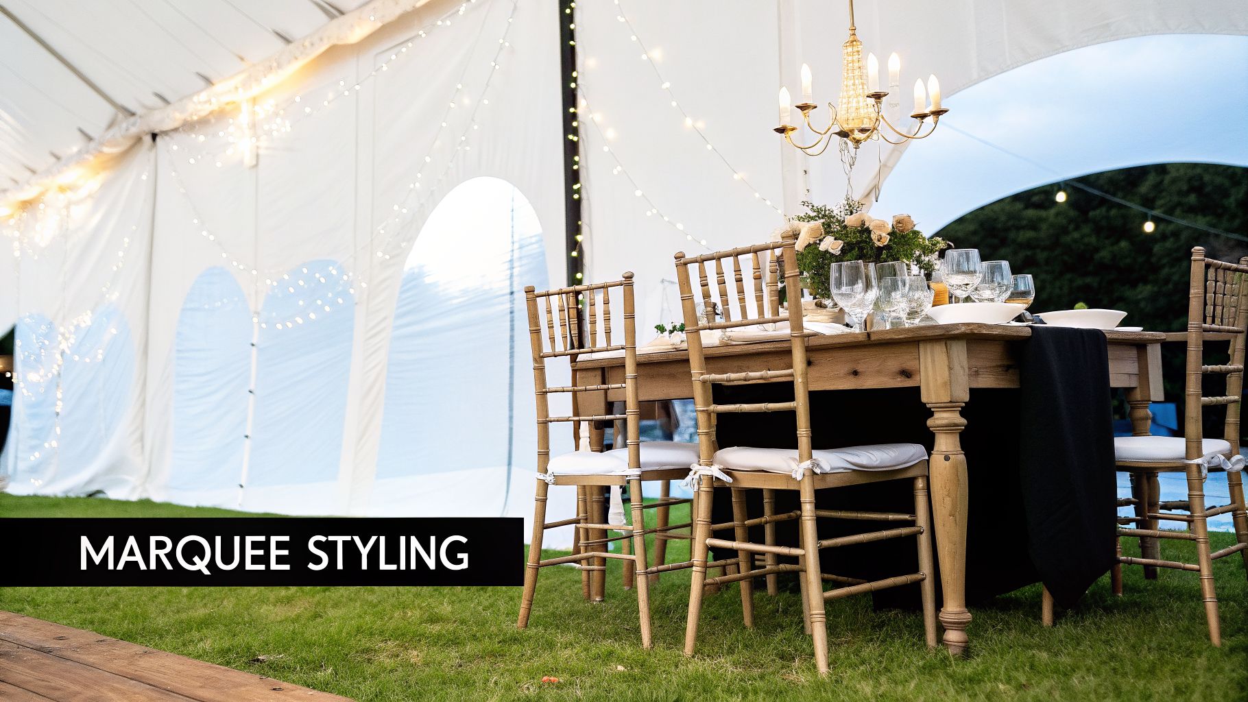 Elegant outdoor wedding marquee with a rustic dining table, chandelier, fairy lights, and floral decor.