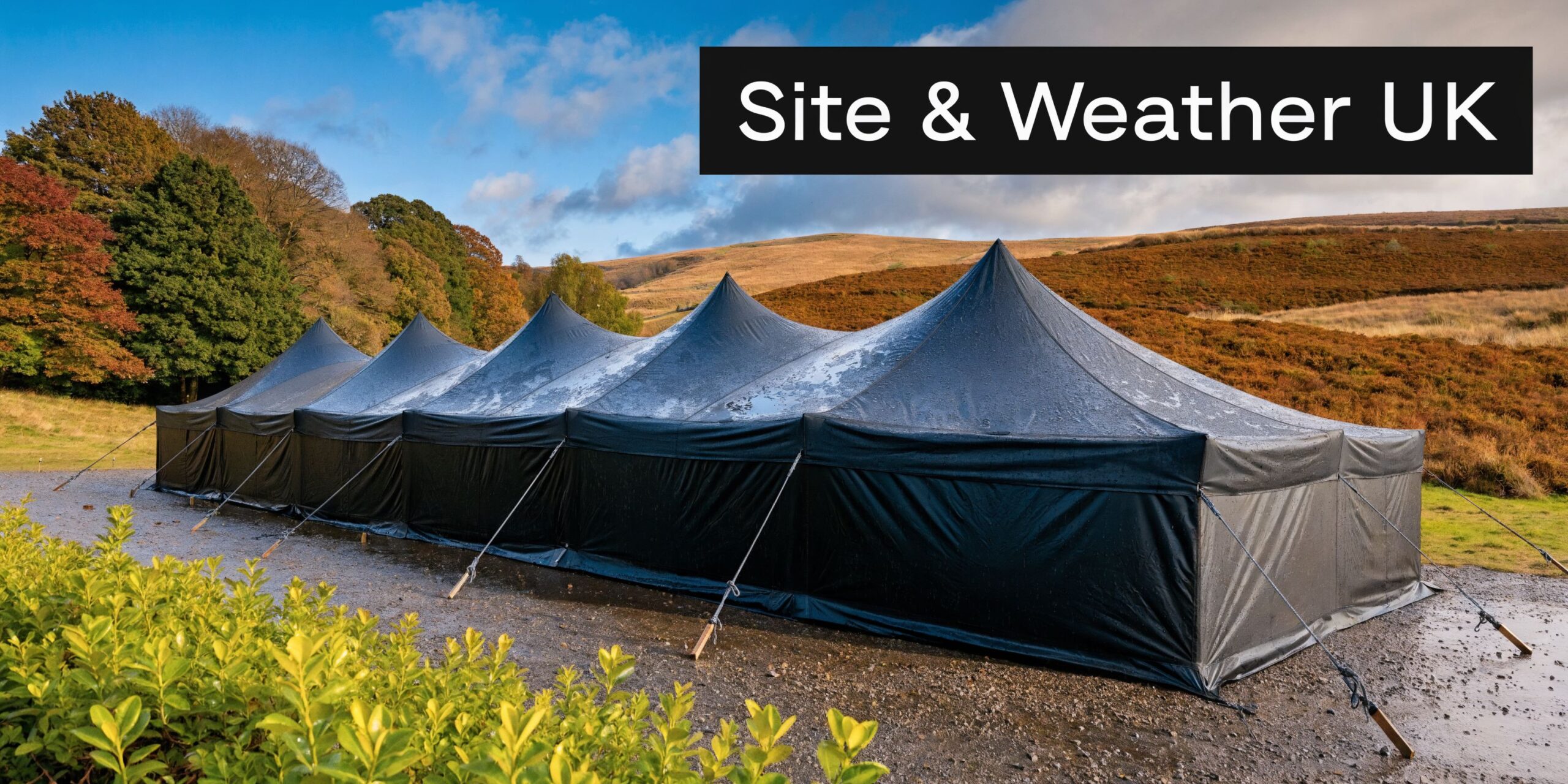 A large black marquee tent set up on a wet gravel surface in a scenic UK landscape.