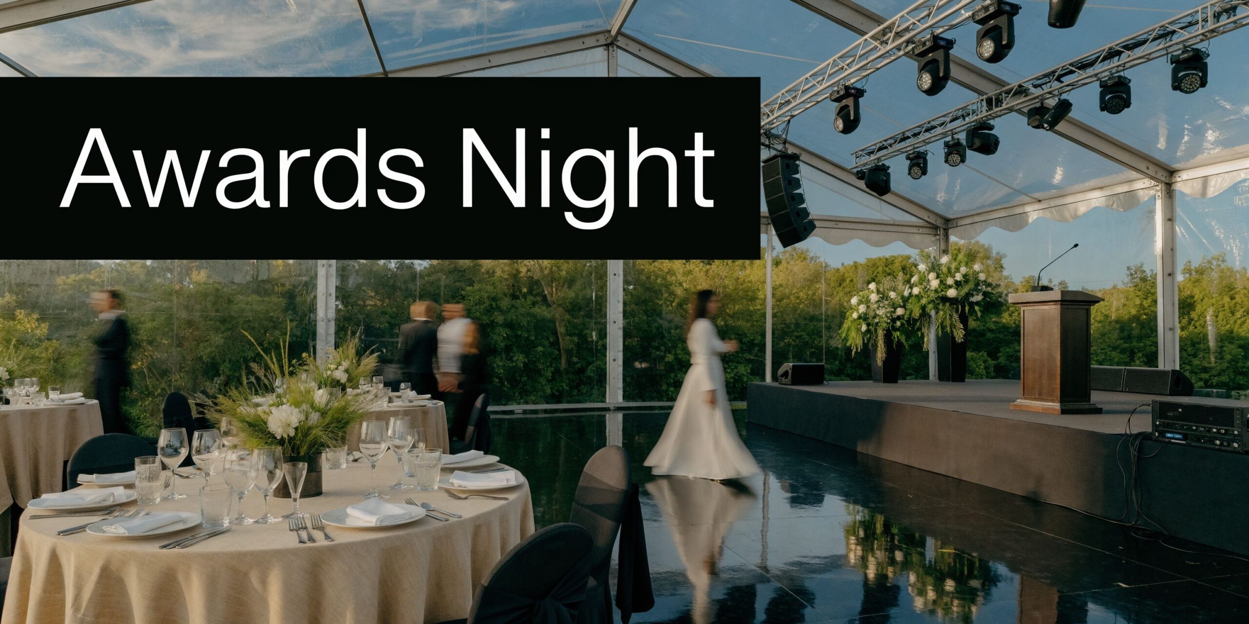 An elegant outdoor tent set up for an awards night event with dining tables and a stage.