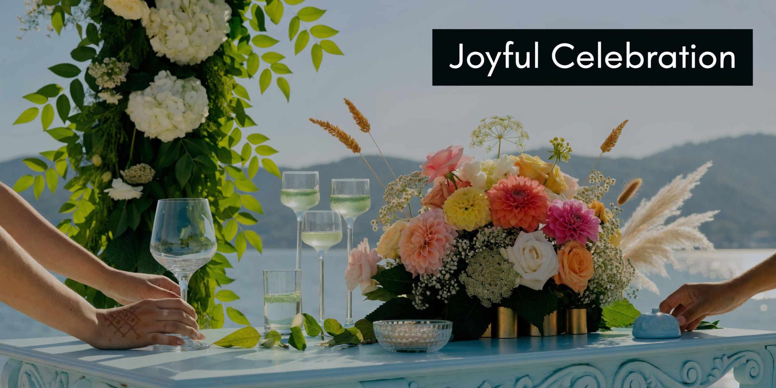 A couple participating in a beautiful outdoor wedding celebration with floral decorations and glasses near water.