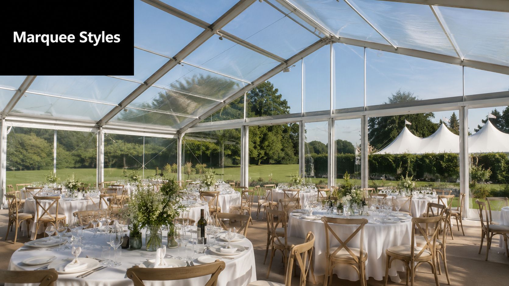 A bright marquee with clear walls and ceiling, set up for a formal outdoor dining event.